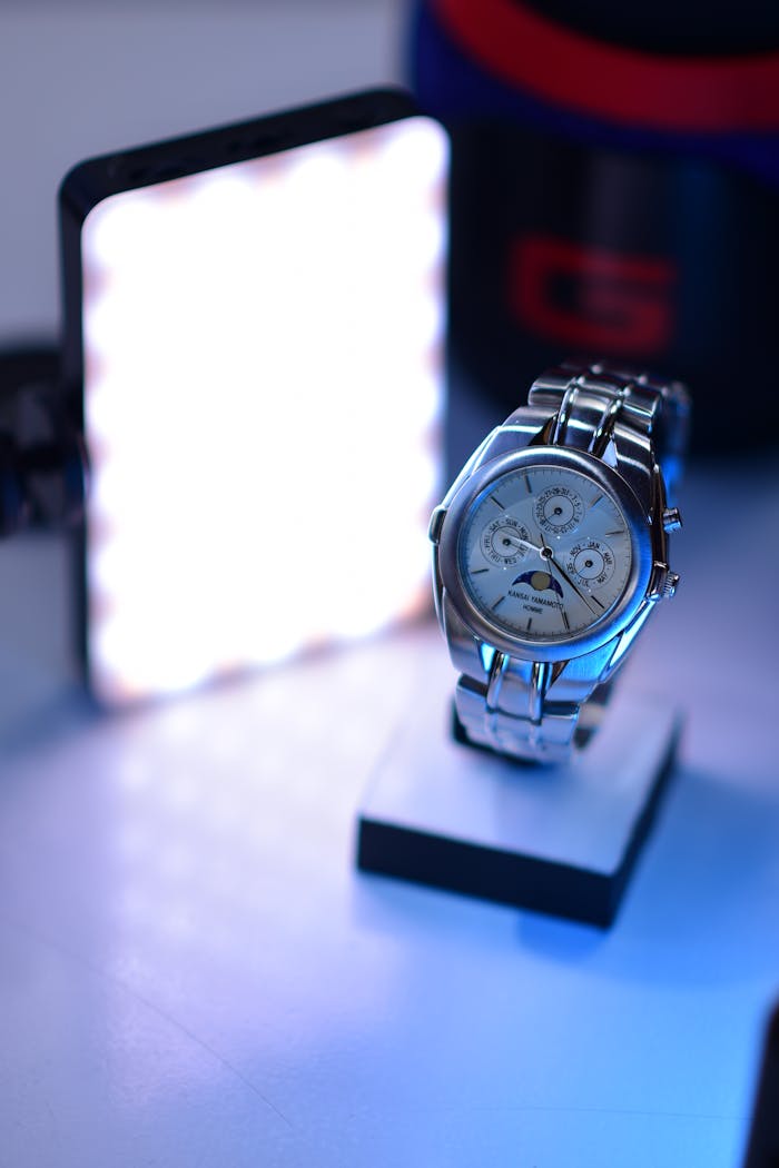 Close-up of a silver watch on display, illuminated by a bright studio light.
